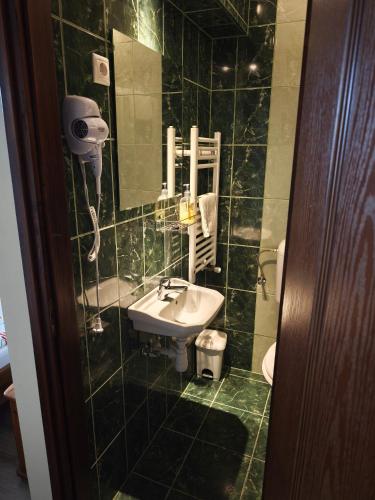 a green tiled bathroom with a sink and a mirror at Magdaléna Vendégház in Hajdúszoboszló