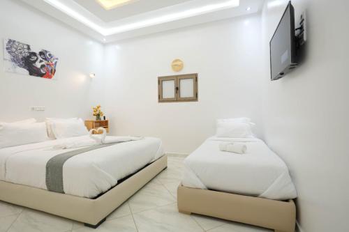 two beds in a white room with a flat screen tv at Hotel apartment america in Dakhla