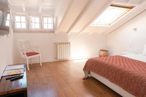 a bedroom with a bed and a chair and a window at Casa das Aguarelas in Ericeira