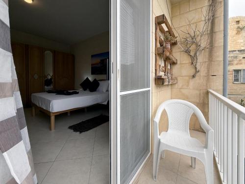a bedroom with a bed and a white chair at Traditional Maltese 3BD Apartment with Front & Back Balconies - Close to Gozo Ferry in Nadur
