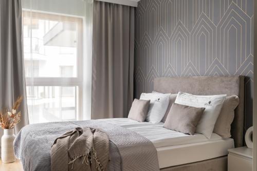 ein Schlafzimmer mit einem Bett mit weißen Kissen und einem Fenster in der Unterkunft Porto Letnica Apartments with Gym & Parking by Lion Apartments in Danzig