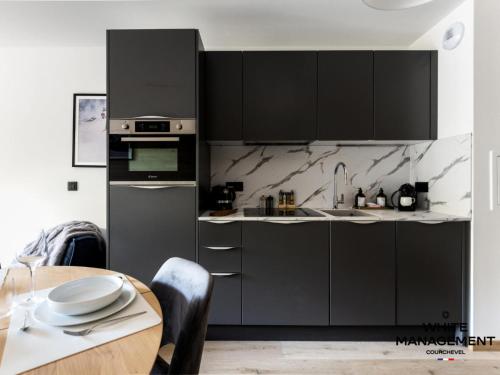une cuisine avec des armoires noires et une table en bois dans l'établissement Résidence Ariondaz Campanule - Superbe appartement familial MAE-8354, à Courchevel