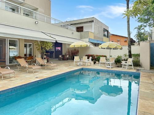 a swimming pool with chairs and umbrellas next to a house at Piscina - 200m do mar - AC - 1 Suite com banheiro in Guarujá