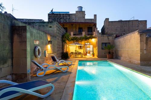 a swimming pool with two chairs next to a building at Tal-Masklu farmhouse in Għarb