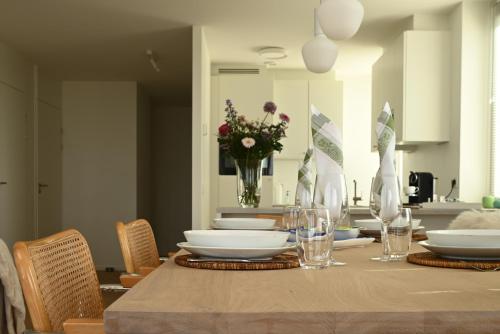 a dining room table with plates and a vase of flowers at Panorama by Villa Mer, Luxury apartment with two bathrooms, two balconies and stunning sea view in Cadzand