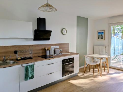 a kitchen with white cabinets and a sink and a table at Ti Malo - studio proche plage Dunkerque in Dunkerque