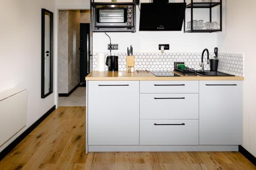 a kitchen with white cabinets and a wooden floor at Apartament LOFT in Rzeszów