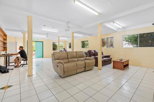 a man sitting at a desk in a room with a couch at Mangoes Backpacker Hostel & Farmstay in Bowen
