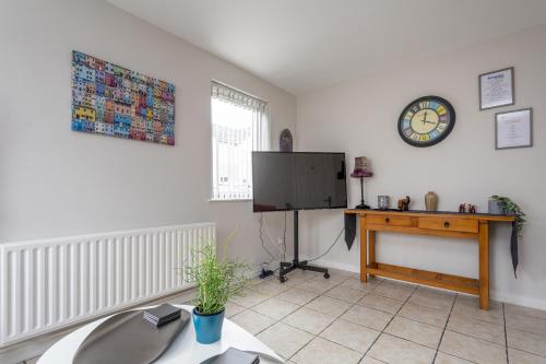 a living room with a tv and a table and a clock at Kings Lodge Apartment & Patio in Belfast