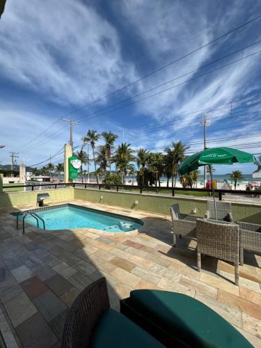 a swimming pool with two chairs and a green umbrella at Hotel Vicino al Mare - Frente mar in Guarujá