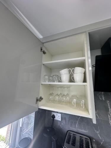 a kitchen cabinet with glasses and dishes on it at Flat in London in Uxbridge