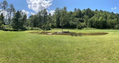 a green field with a pond in the middle at Sunny 2BR with Pond, Fireplace, Walk to Stowe in Stowe