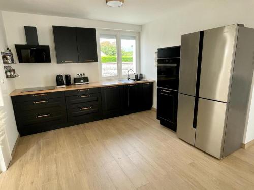 une cuisine avec des armoires noires et un réfrigérateur en acier inoxydable dans l'établissement Villa Rénovée 3 Chambres, Proche Plage avec WiFi, Ménage et Linge Inclus - FR-1-323-507, à Saint-Hilaire-de-Riez