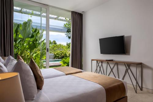 a bedroom with a bed and a tv and a window at Hideaway Villas Bali - Uluwatu by Kanaan Hospitality in Uluwatu