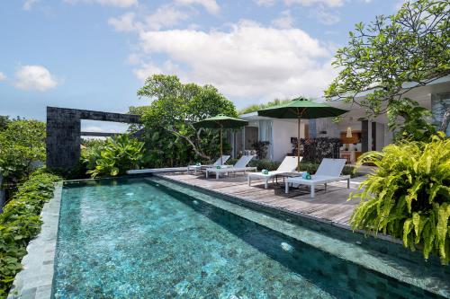 a pool with chairs and umbrellas next to a house at Hideaway Villas Bali - Uluwatu by Kanaan Hospitality in Uluwatu