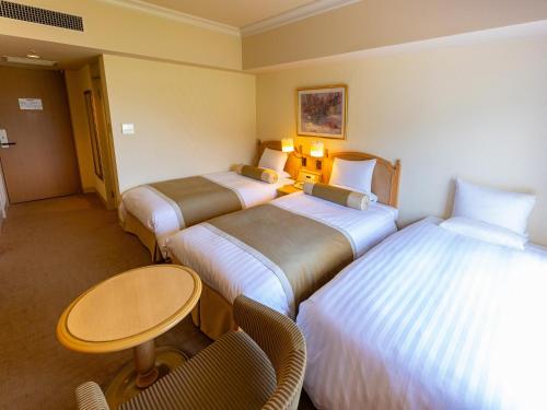 a hotel room with three beds and a table and chairs at Hotel Okura JR Huis Ten Bosch in Sasebo