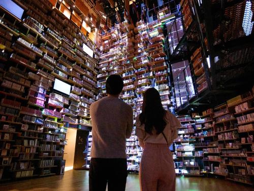 a man and woman standing in front of a library of books at IN THE LIBRARY hotel and books TOKOROZAWA - Opening in 15th July 2025 in Tokorozawa