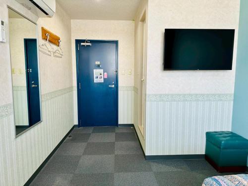a hallway with a blue door and a flat screen tv at Station Business Hotel Tenshukaku in Hitoyoshi