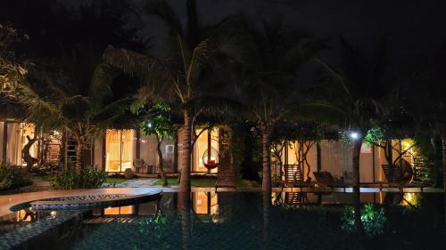 a pool at night with palm trees in front of a building at An Hoa Residence in Long Hai