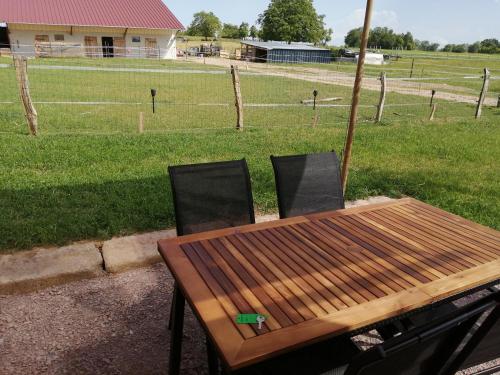 a wooden table with two chairs and a field at Le Lodge de la Hutt' aux animaux 