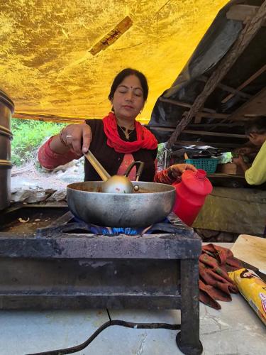 a woman cooking food in a bowl on a stove at Blabla House Himachal in Pulga