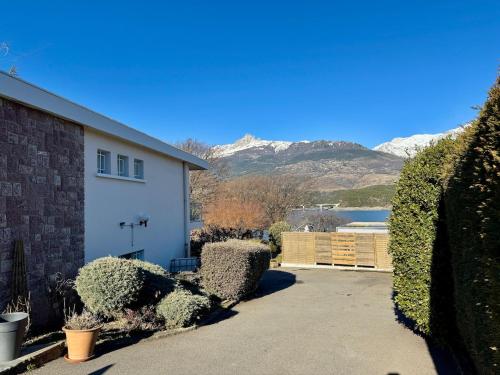 a house with a driveway with bushes and mountains in the background at Villa unique, 50 mètres du jardin au lac in Savines