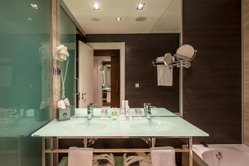 a bathroom with a sink and a mirror and a tub at Hotel Diagonal Plaza in Zaragoza