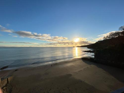 a beach with the sun shining on the water at Harbour Stays - The Marine Centre, Saundersfoot Harbour, SA69 9HE in Saundersfoot