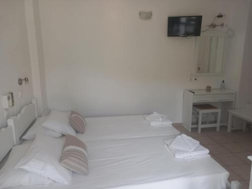 a white bedroom with two beds and a television at Studios Margarita in Platis Yialos Sifnos
