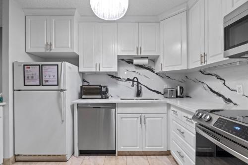 a white kitchen with white cabinets and a refrigerator at Modern 2 bedroom next to Stampede, 17th w Parking in Calgary