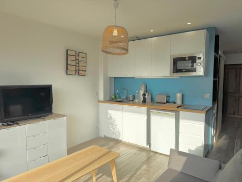 Il comprend une cuisine avec des placards blancs, une télévision et une table. dans l'établissement Appartement face à la mer, à Saint-Raphaël