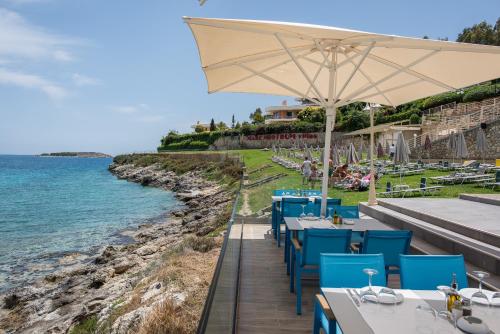a restaurant with blue chairs and an umbrella next to the water at Mare Nostrum Villas in Marathi