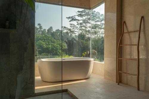 a bath tub in a bathroom with a large window at The Lumbung Jaya Resort in Tegalalang