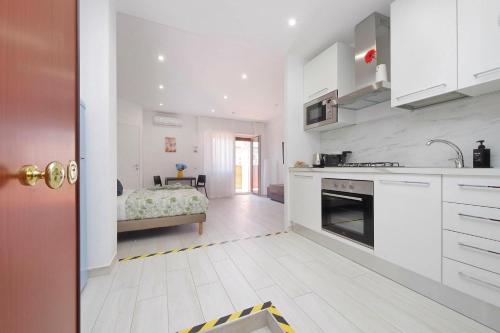 a kitchen with white cabinets and a bed in the background at Attico con balcone - Mare e Comfort in Lido di Ostia