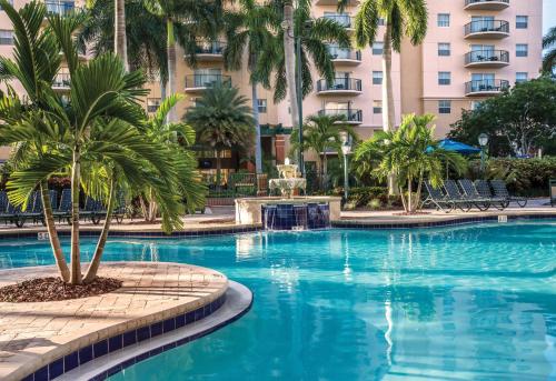 a swimming pool with palm trees in front of a building at Wyndham Palm-Aire 1BR Apartment with Resort Access in Pompano Beach