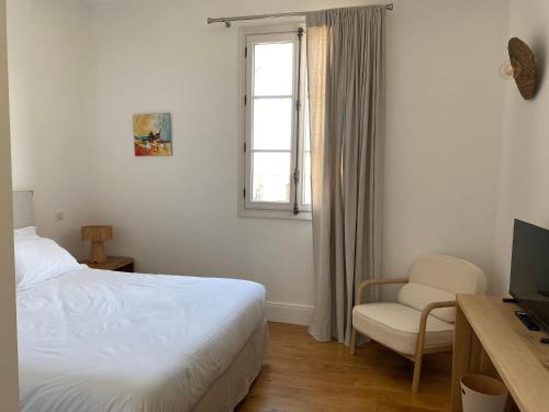 a bedroom with a bed and a chair and a window at La Hugotine in Marseillan
