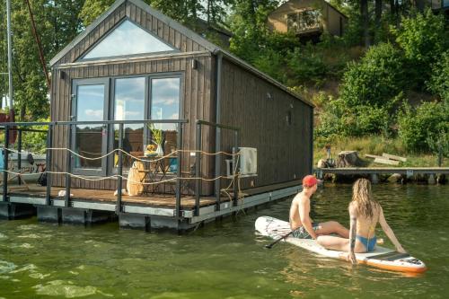 two people on a paddle board in the water with a house at Ruciane Park - Mazury resort & spa in Ruciane-Nida