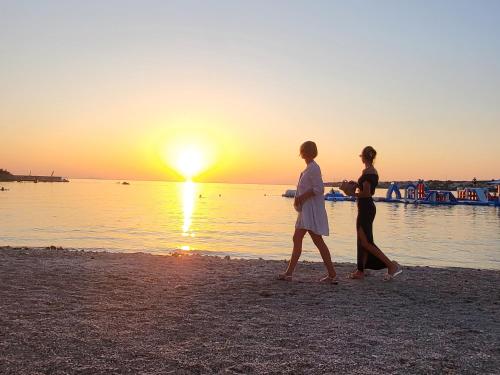 two people walking on the beach at sunset at Apartman Dalmatino in Petrcane