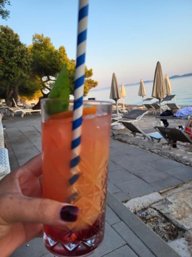 a hand holding a drink with a striped straw at Apartman Dalmatino in Petrcane
