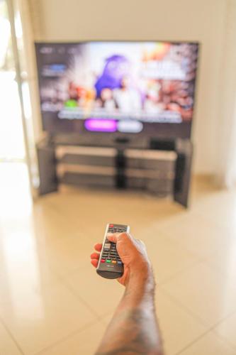 a person holding a remote control in front of a tv at Villa Ile d'Eden - Vue mer-Piscine - By Sister Home in Sainte-Marie