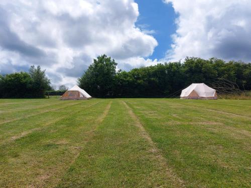 two tents in a grassy field with trees at Hopgarden Glamping and camping - Luxury furnished Bell tents & Shepherd huts plus camp field to pitch your own tents in Wadhurst