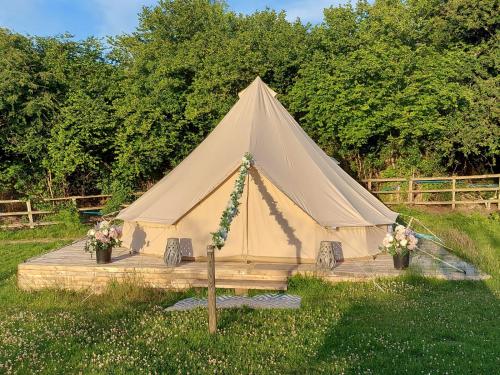 a tent in a field with flowers at Hopgarden Glamping and camping - Luxury furnished Bell tents & Shepherd huts plus camp field to pitch your own tents in Wadhurst