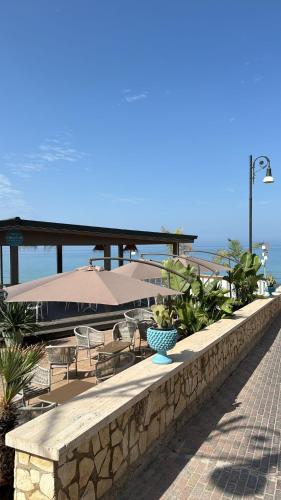 a stone wall with chairs and tables and umbrellas at Paguro Beach Hotel in Siculiana Marina