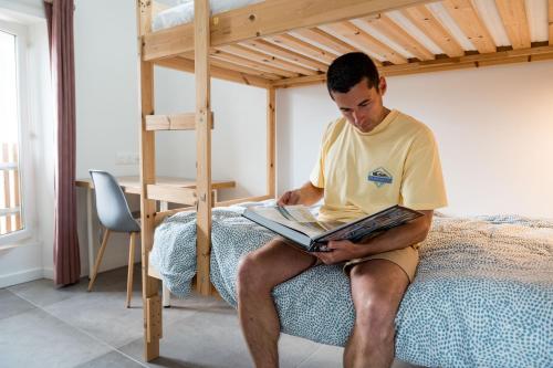 a man sitting on a bed reading a book at Ted Surf House in Capbreton