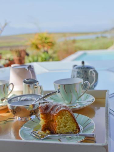 a piece of cake on a plate with cups on a table at Vineyard Views Country House in Riebeek-Kasteel