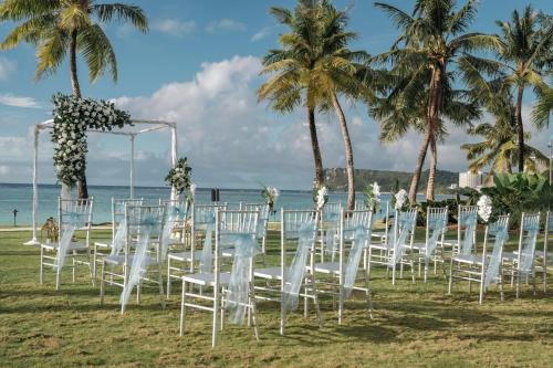a row of white chairs on the beach with palm trees at Crowne Plaza Resort Guam in Tumon