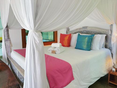 a bedroom with a white canopy bed with colorful pillows at Hotel Vila Kebaya in Ilhabela