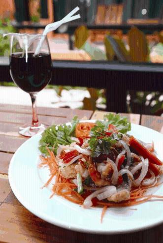 a plate of food on a table with a glass of wine at The Shambhala Khaolak Resort in Khao Lak