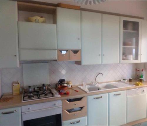 cocina con armarios blancos, fogones y fregadero en Splendido appartamento a Soverato fronte mare, en Soverato Marina