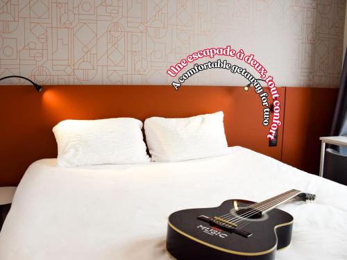 une guitare sur un lit avec un panneau sur le mur dans l'établissement ibis Rodez Centre, à Rodez